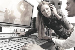 Popzenész, aki fejhallgatón hallgat zenét egy hangstúdióban, miközben producerként videót néz a plazmaképernyőn